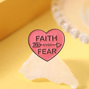 Macro shot of pink enamel heart brooch with Faith over Fear text on yellow backdrop