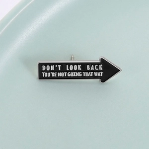 Detailed close-up of a black arrow enamel pin with Don't Look Back motivational text