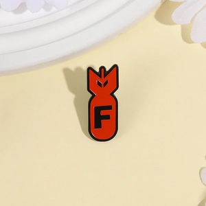 Vibrant red bomb-shaped enamel pin with black letter F on a warm aesthetic background
