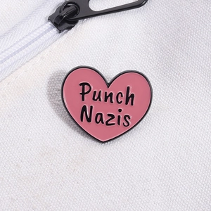 Detail of pink heart-shaped enamel pin with Punch Nazis text on white canvas bag