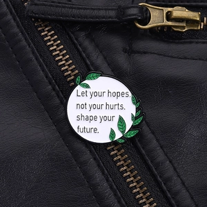 Détail d'une broche en émail blanc épinglée sur une veste en cuir noir avec citation
