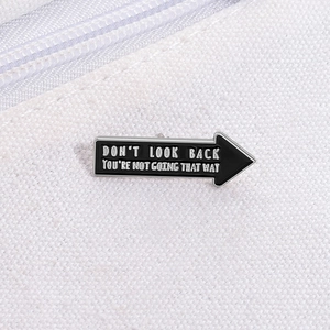 Detail of arrow enamel pin on white canvas with motivational quote Don't Look Back