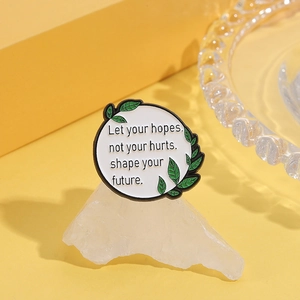 Détail d'une broche en émail ronde avec motifs floraux et citation sur socle en pierre