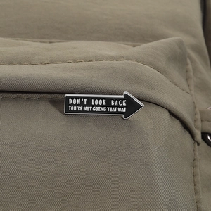 Close-up of arrow enamel pin with motivational text on khaki backpack material