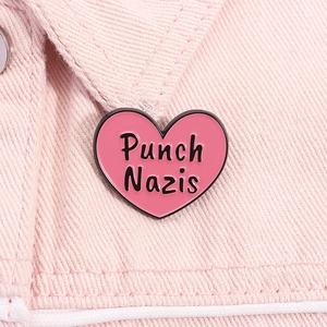 Detail of pink heart enamel pin with black text on light pink denim jacket fabric