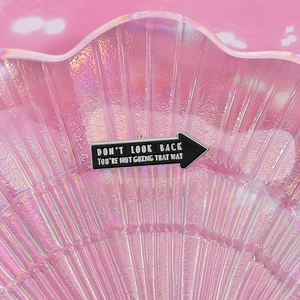 Macro shot of arrow enamel pin with 'DON'T LOOK BACK' text on pink iridescent tray