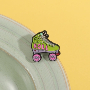 Detail of retro roller skate enamel pin with 'This Is How I Roll' slogan on yellow background