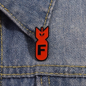 Detailed close-up of a red bomb-shaped enamel pin with letter F on blue denim fabric