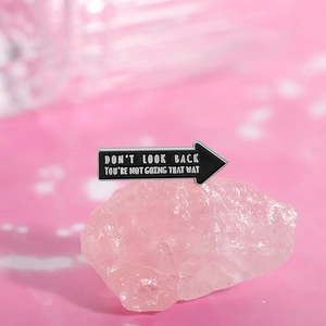 Detail of arrow enamel pin with white text on pink mineral rock decorative background