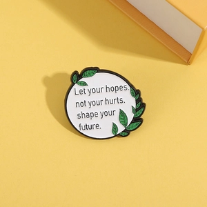 Round enamel brooch with green leaf detail and inspirational quote on yellow background