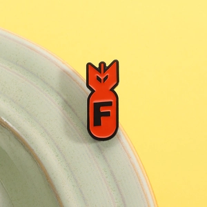 Macro view of red enamel F-bomb pin badge showing the glossy zinc alloy finish