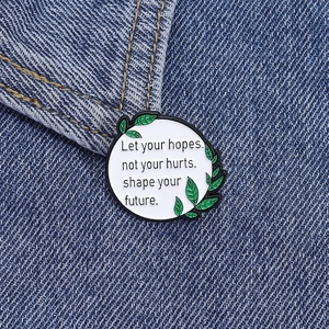 Broche en émail aux feuilles vertes avec citation sur une veste en denim bleu