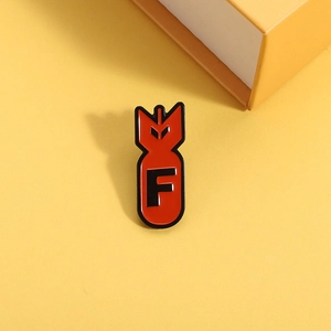 Cartoon red enamel bomb-shaped pin with black letter F over a bright yellow background