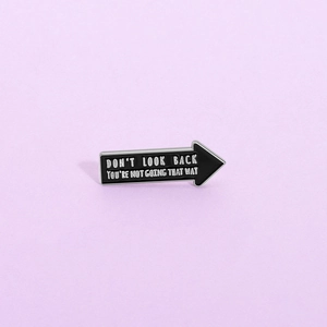 Detailed view of arrow-shaped enamel pin with motivational text on purple background