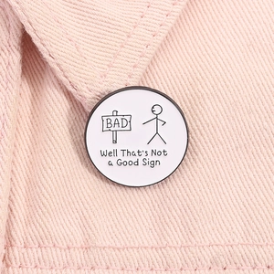 Detail of stick figure enamel pin with 'Not a Good Sign' text on pink denim fabric