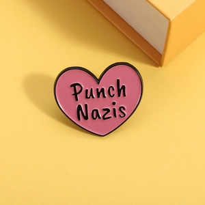 Pink heart-shaped enamel brooch with black 'Punch Nazis' slogan on a yellow background