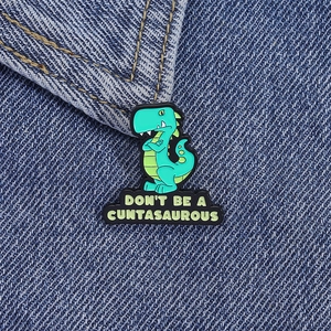 Dettaglio di spilla in smalto con dinosauro e slogan su giacca di jeans blu