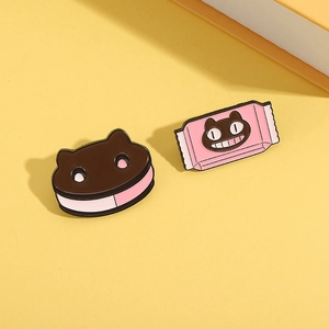 Close-up of cat-shaped cookie and pink candy box enamel pins on yellow background