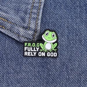 Groene emaille kikker pin badge met tekst Fully Rely On God gepind op blauwe denim