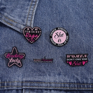 Nahaufnahme von fünf feministischen Emaille-Pins auf Denim mit rosa-lila Empowerment-Slogans