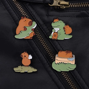 Detail of four enamel pins featuring cute capybara and crocodile designs on leather