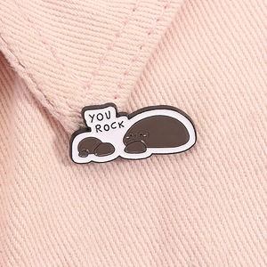 Macro detail of enamel brooch with two brown seals and YOU ROCK text on pink denim fabric