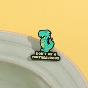 Funny green dinosaur enamel pin with bold quote on ceramic bowl rim with yellow backdrop