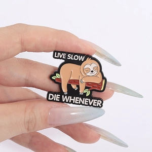 Macro shot of sloth enamel pin with text Live Slow Die Whenever held in hand