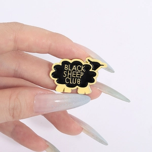 Broche créative en émail mouton noir avec lettrage doré Black Sheep Club sur fond blanc