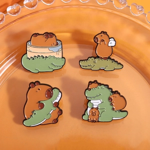 Close-up of four cute capybara and crocodile enamel pins displayed on an orange tray