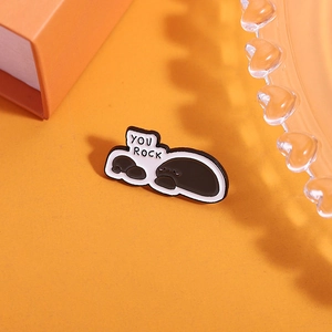 Detailed close-up of a grey stone enamel pin with You Rock text on an orange background