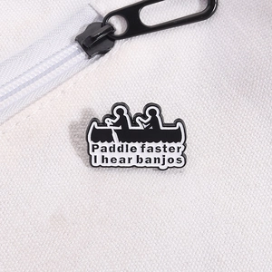 Close-up of black enamel banjo pin with funny paddle faster quote on white canvas bag