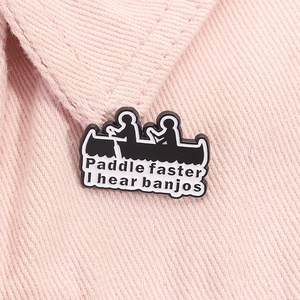 Detail of Paddle Faster I Hear Banjos enamel pin on pink denim fabric with sharp focus