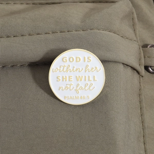 Détail de la broche ronde en émail avec bordure dorée et citation sur toile marron