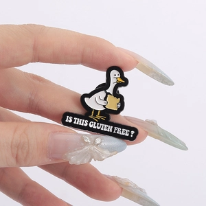 Detail showing hand holding an enamel duck brooch with Is This Gluten Free text