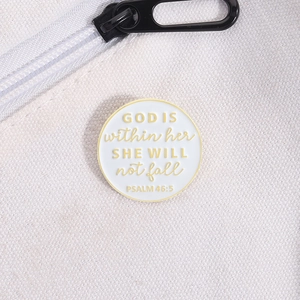 Gros plan d'une broche en émail avec citation de Psaume 46:5 sur un fond en toile blanc