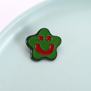 Close-up of a green star enamel pin with a cute red smiley face on a ceramic surface