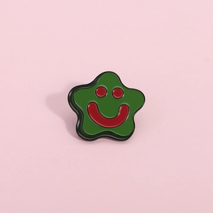 Close-up of green star-shaped enamel pin with red smiley face and black metallic edges