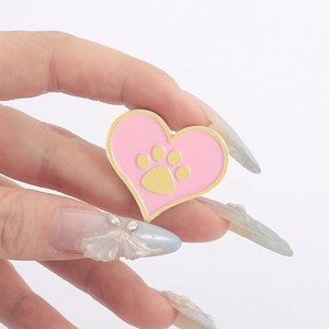 Gros plan détaillé d'un pin's en émail cœur rose avec un motif de patte de chat dorée