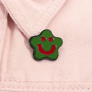 Close-up of green star-shaped smiley face enamel pin on pink textured fabric