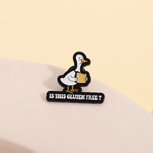 Gros plan d'un pin's en émail canard avec le texte 'Is this gluten free?' sur fond beige