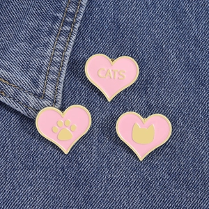 Vue détaillée de trois épingles en émail cœur rose pour chat sur tissu en jean bleu