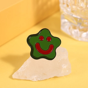 Macro shot of a green star-shaped enamel brooch with a red smiley face on white stone