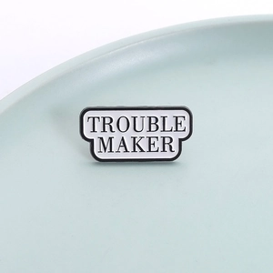 Minimalist enamel Trouble Maker brooch pin with bold black lettering on white background