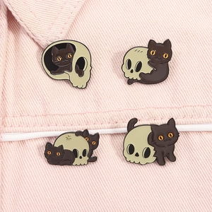Détail de quatre épingles en émail chat noir et crâne sur fond en jean rose pastel