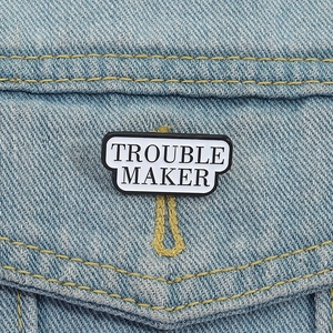 Macro view of Trouble Maker enamel pin attached to a blue denim jacket pocket