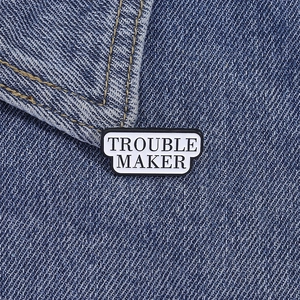 Detail of Trouble Maker enamel pin badge on dark blue denim fabric texture