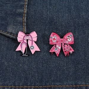 Detail of pink bow enamel pins with medical symbols pinned on blue denim fabric