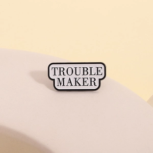 Minimalist alloy enamel pin with Trouble Maker text on a warm beige background