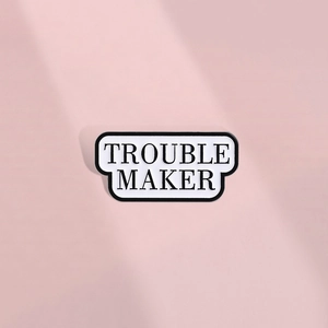 Detail shot of the black and white enamel pin with bold Trouble Maker text